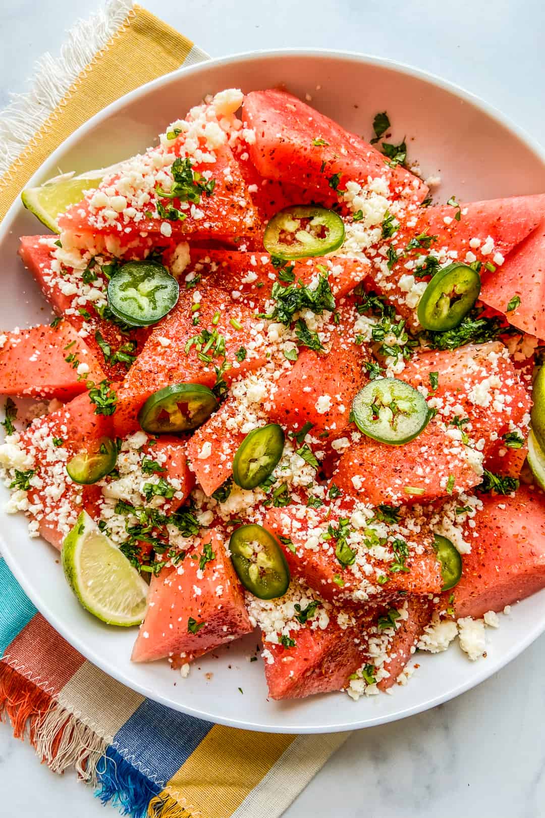 Mexican watermelon salad in a large white bowl on a colorful napkin.