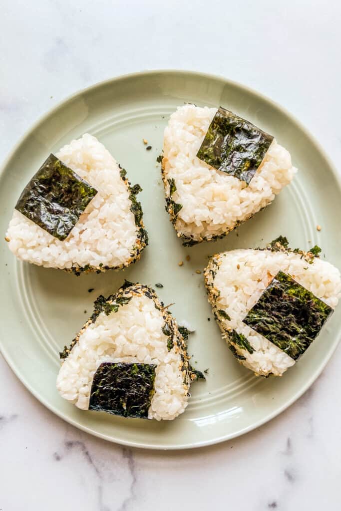 Four spicy tuna onigiri sitting on a green plate.