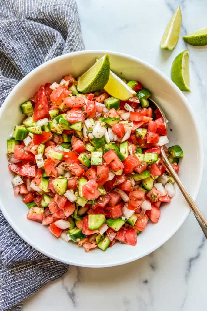 Shirazi salad in a white serving bowl next to a blue napkin and lime slices.