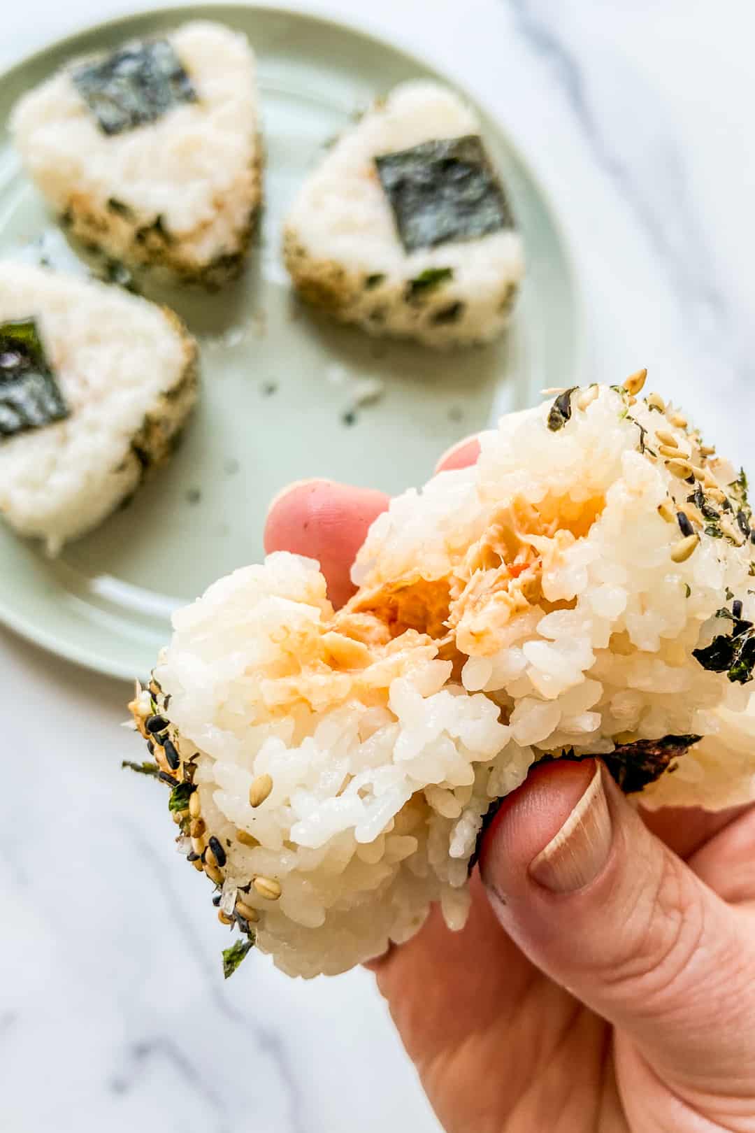 A hand holding an onigiri with a bite taken out of it.