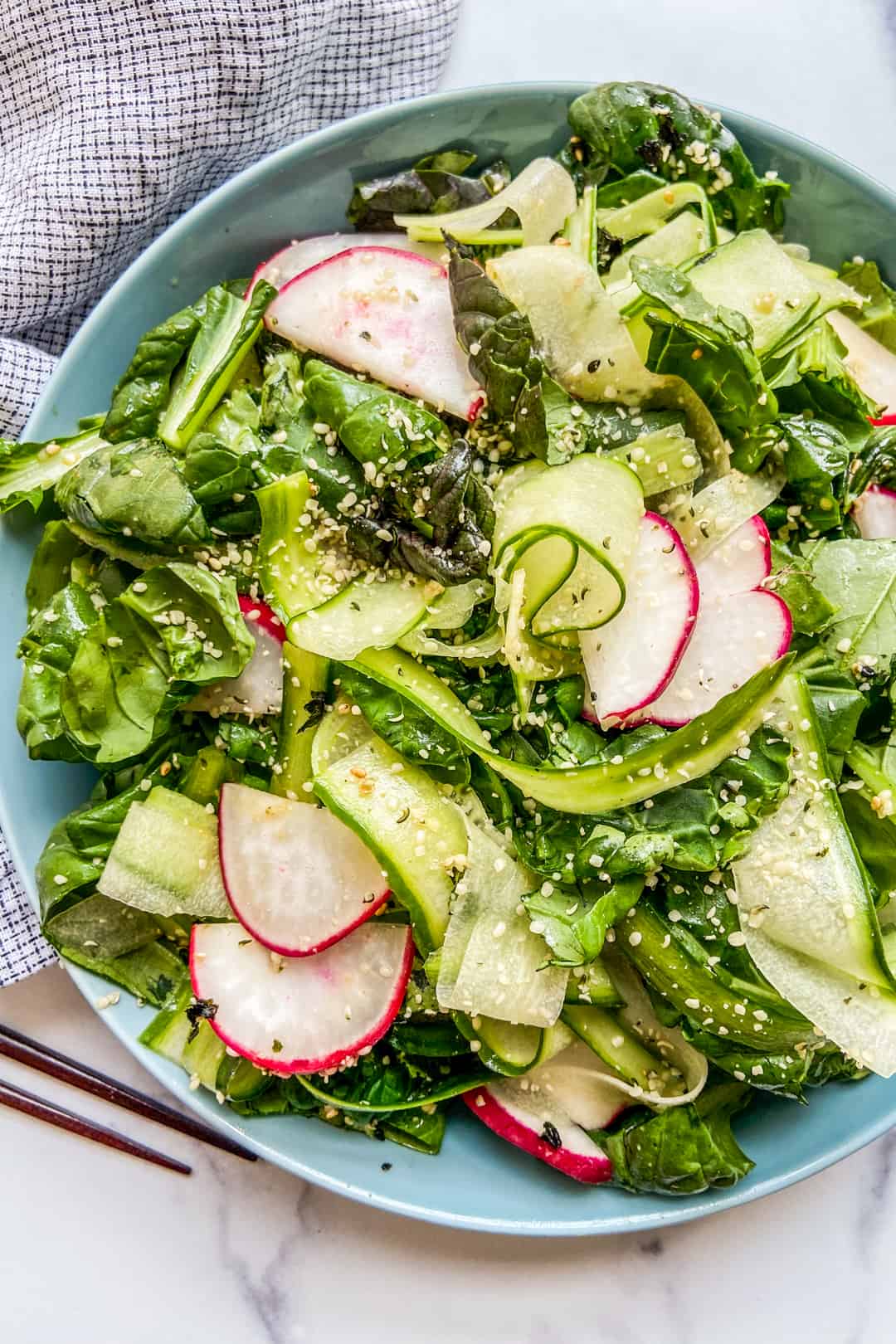 Tatsoi greens salad in a blue serving bowl next to a napkin and chopsticks.