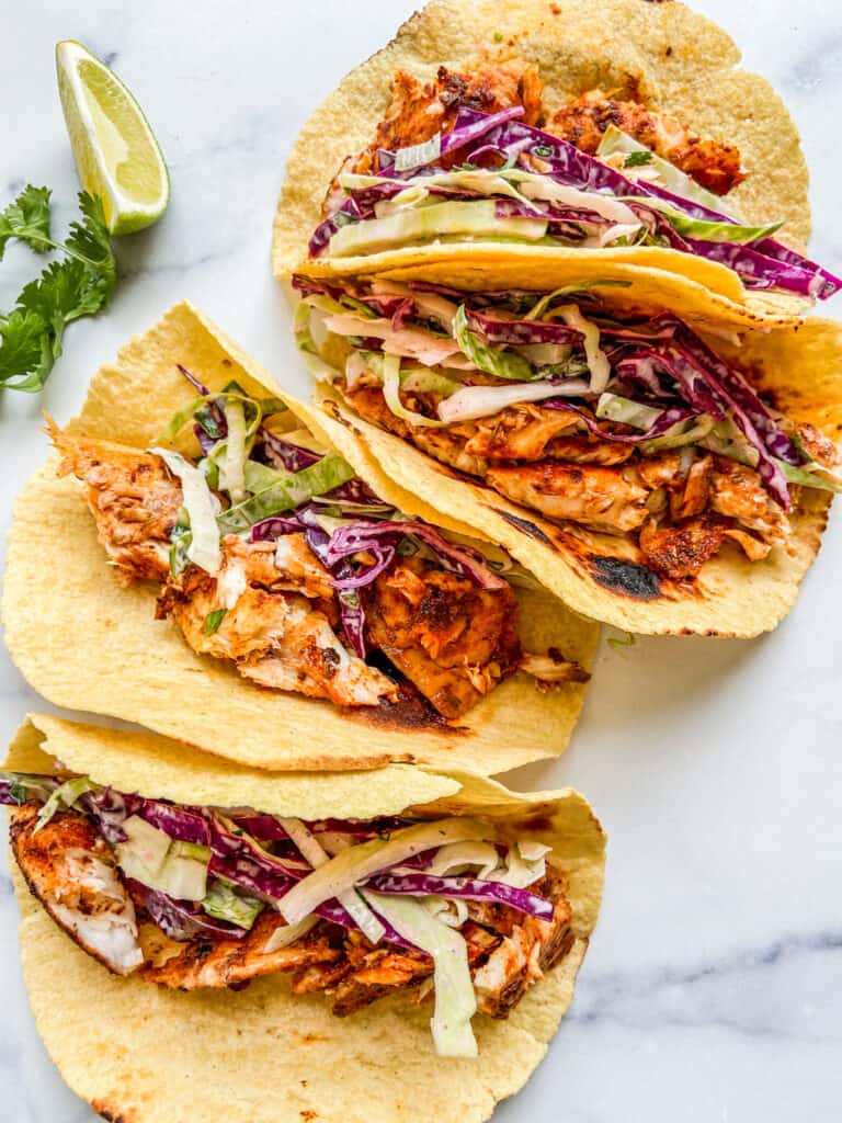 Four tilapia tacos sitting on a marble background.