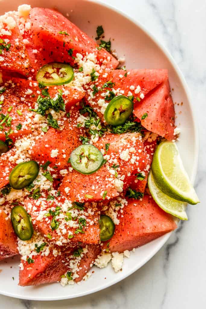 A closeup shot of a watermelon salad topped with tajin, cotija cheese, and jalapenos.
