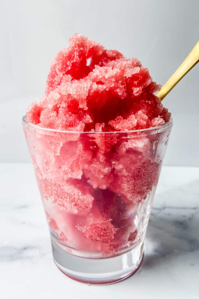 A glass of watermelon sorbet with a gold spoon.