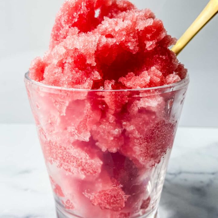 A glass of watermelon sorbet with a gold spoon.