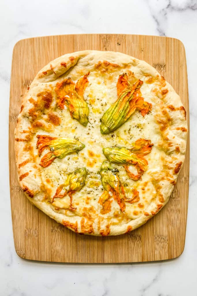 An overhead shot of zucchini flower pizza on a cutting board.