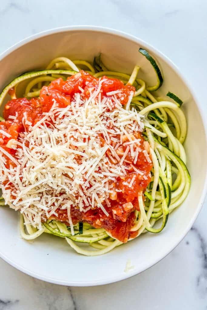 A bowl with zoodles and tomato sauce, topped with parmesan cheese.