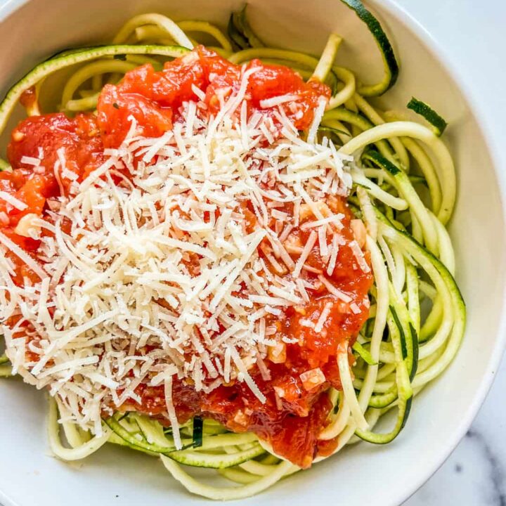 A bowl with zoodles and tomato sauce, topped with parmesan cheese.
