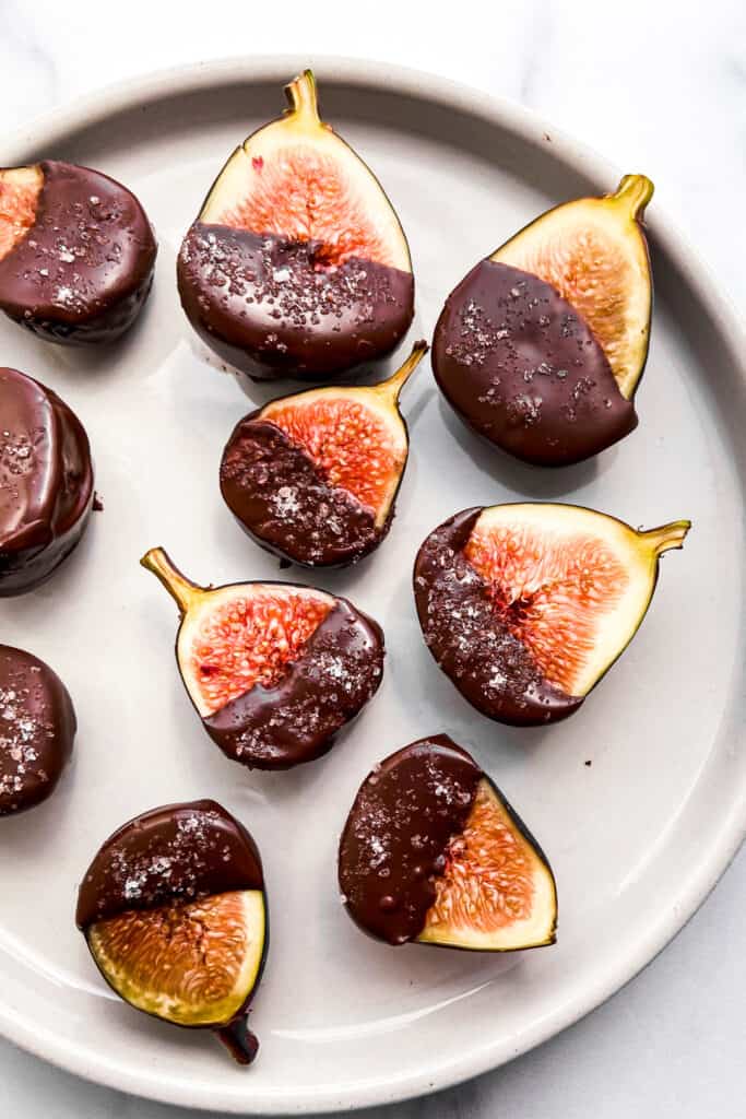 Figs covered in dark chocolate and salt on a small plate.