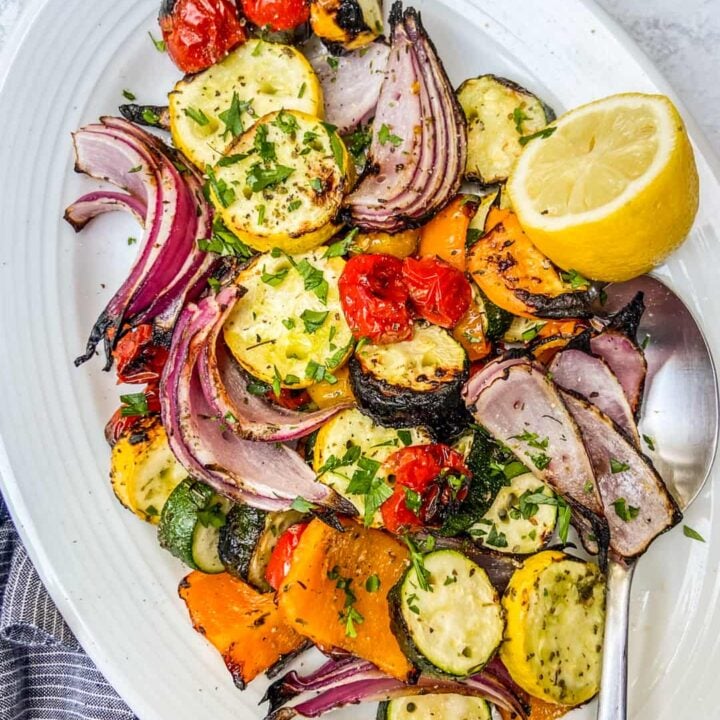 An overhead shot of a platter of grilled vegetables, topped with finely chopped herbs, next to a blue napkin.