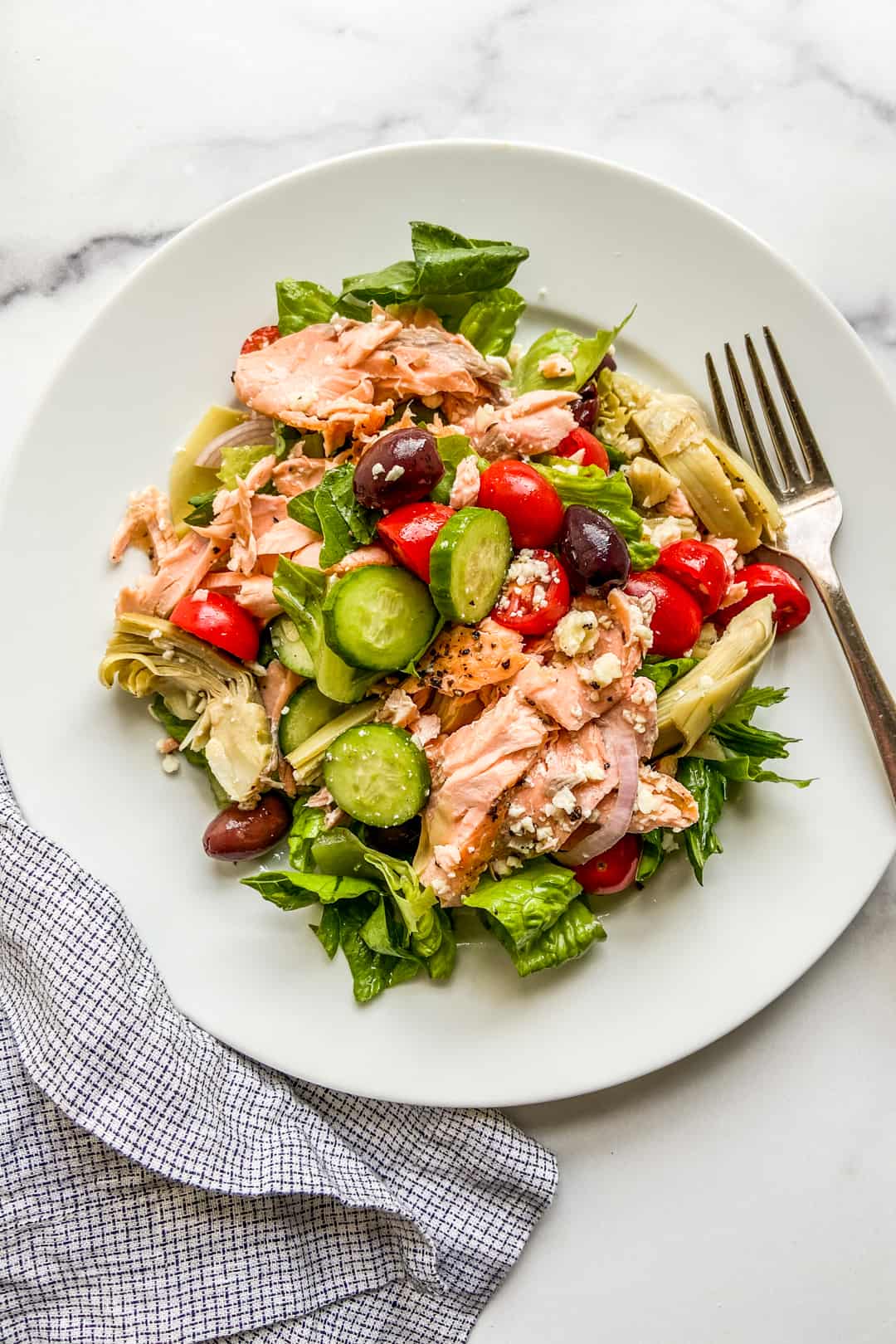 A large white plate with a Mediterranean salmon salad.