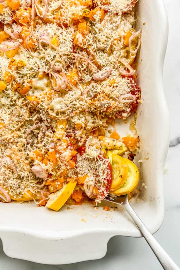 A closeup shot of squash tomato gratin in a baking dish with a silver spoon.