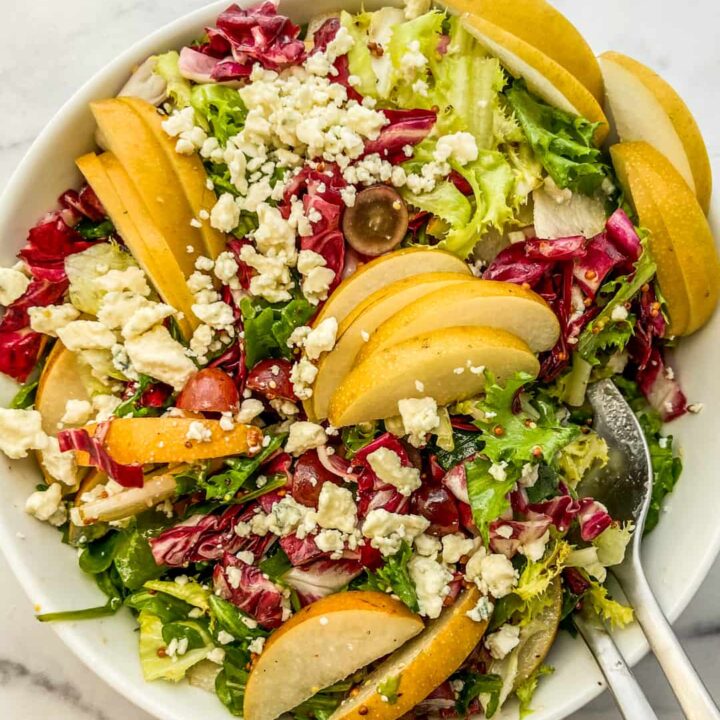 An overhead shot of an Asian pear salad in a white bowl with silver serving spoons.