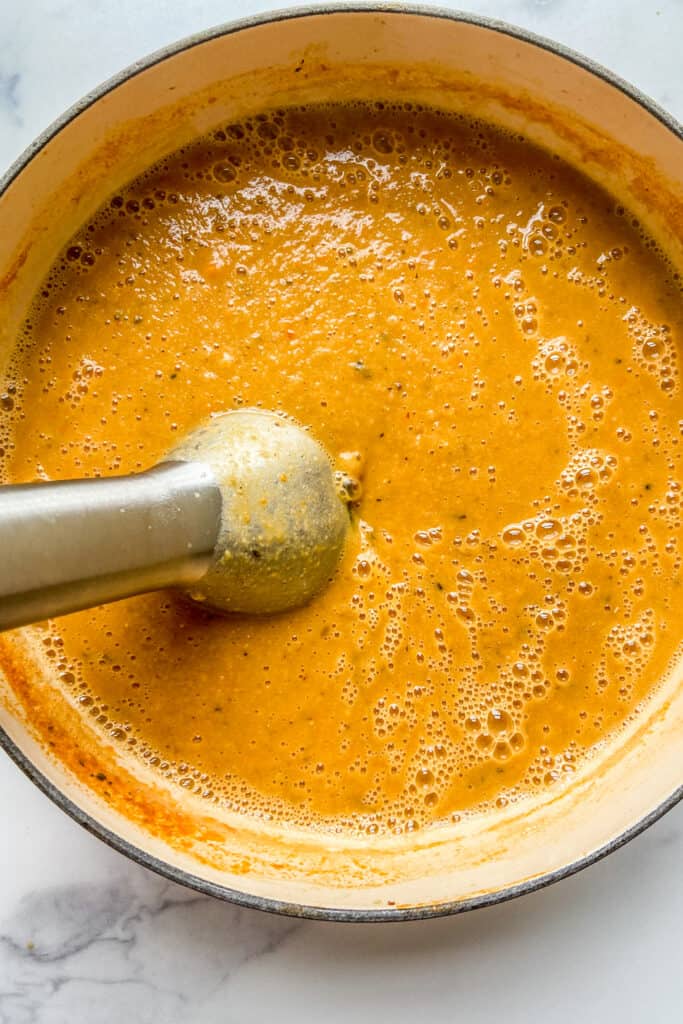 Lentil soup being blended with an immersion blender.