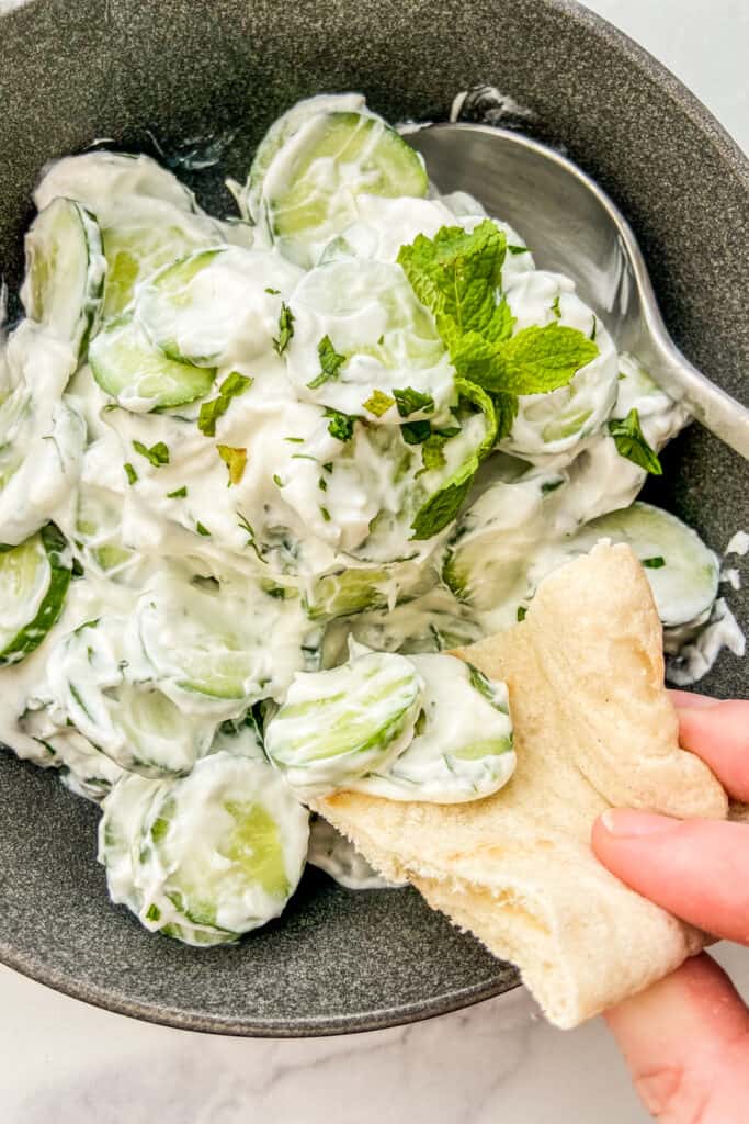 A closeup shot of a piece of pita bread scooping up cucumber yogurt salad.