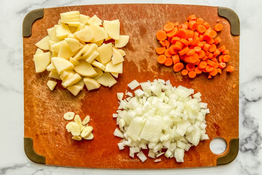 Chopped potatoes, carrots, onion, and garlic on a cutting board.