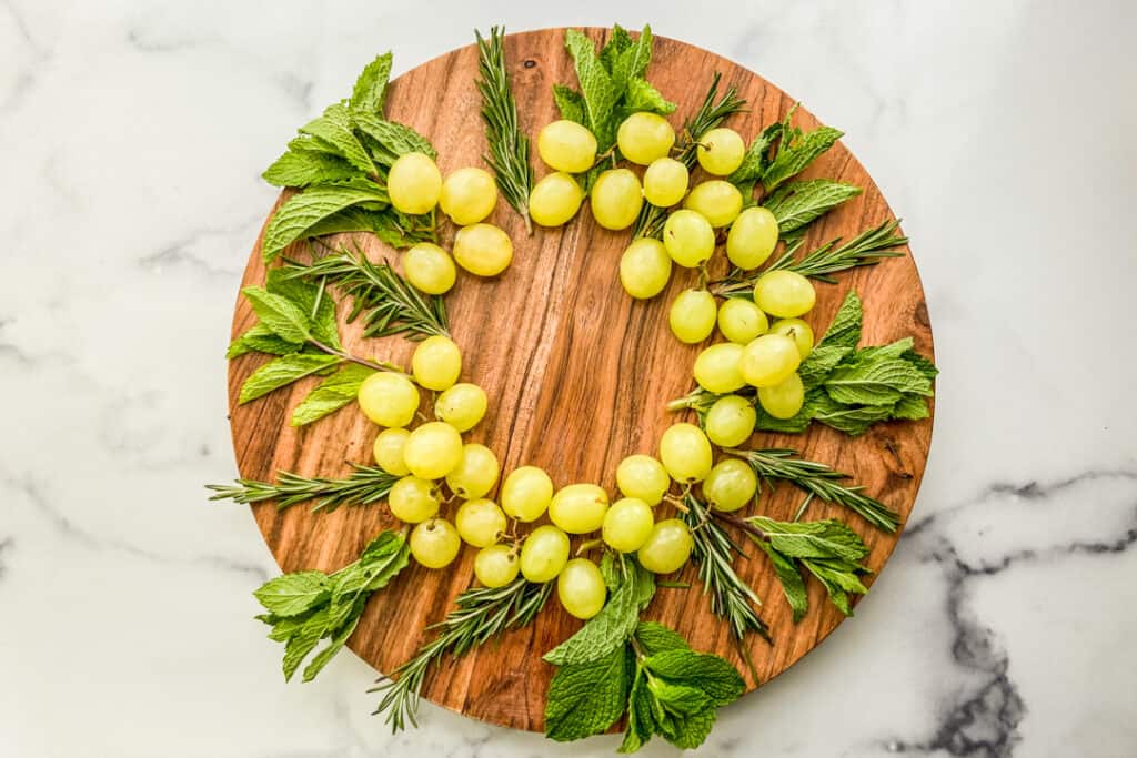 Fresh herbs and green grapes on a large wooden plate.