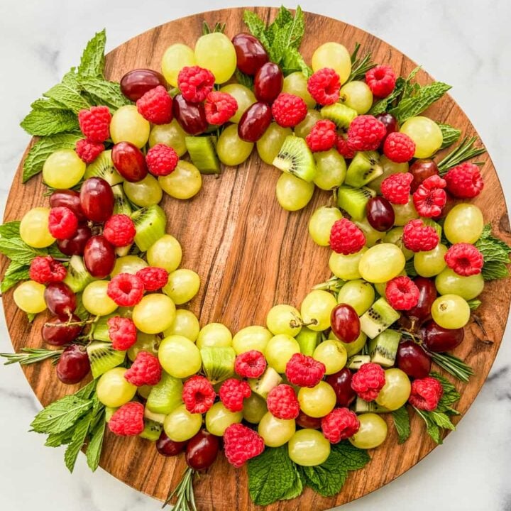 An overhead shot of a Christmas fruit wreath on a large wooden circular plate.