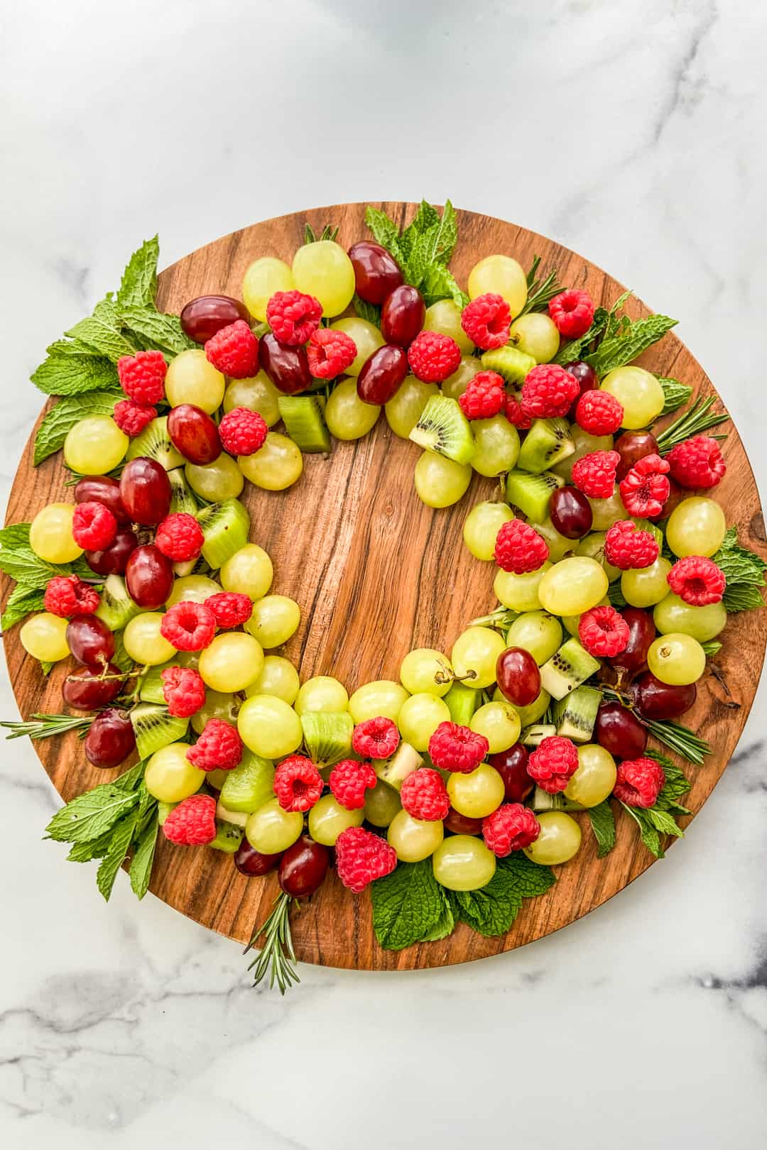 An overhead shot of a Christmas fruit wreath on a large wooden circular plate.