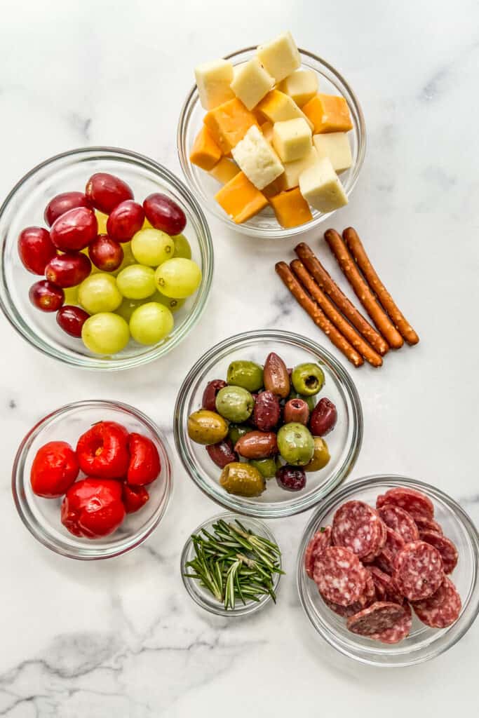 Grapes, cheese, pretzel, olives, salami, and rosemary.