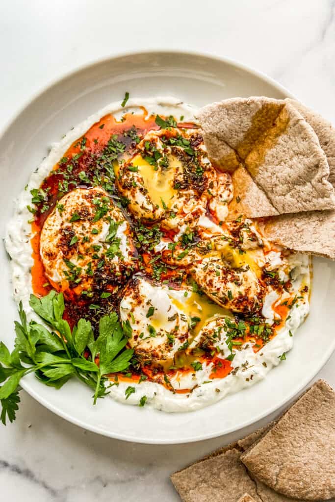 An overhead shot of a bowl of cilbir with some sliced of pita bread.