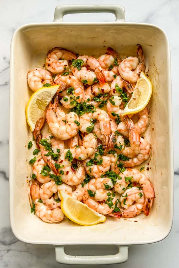 An overhead shot of a baking dish with baked shrimp, topped with parsley, and lemon slices.