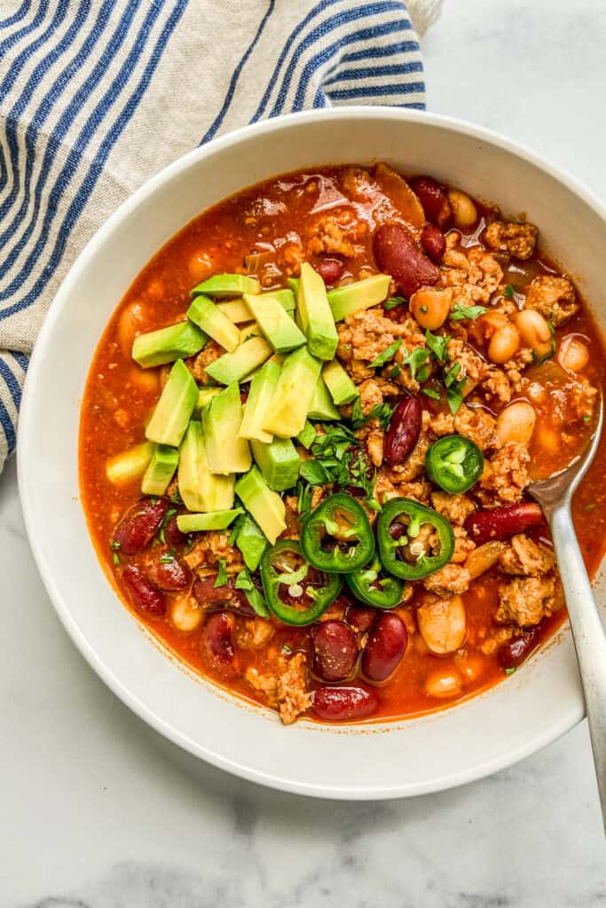 A closeup shot of a bowl of turkey chili, topped with jalapeno and avocado.