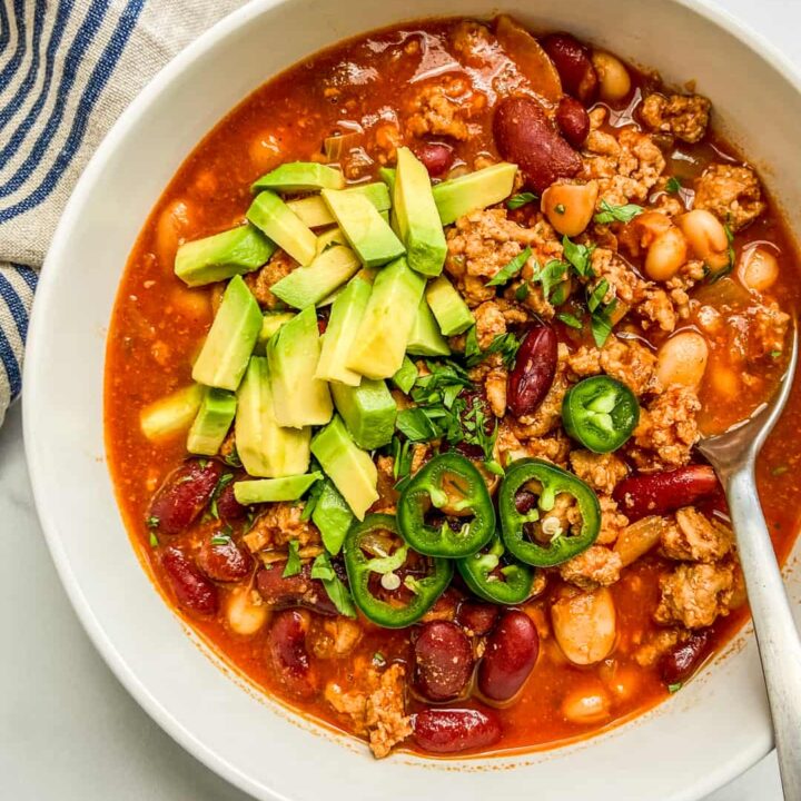A closeup shot of a bowl of turkey chili, topped with jalapeno and avocado.