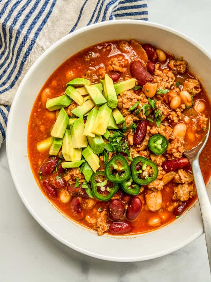 A closeup shot of a bowl of turkey chili, topped with jalapeno and avocado.