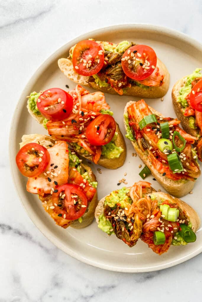 An overhead shot of an off white plate with kimchi avocado toast bites.