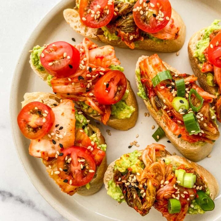 An overhead shot of an off white plate with kimchi avocado toast bites.