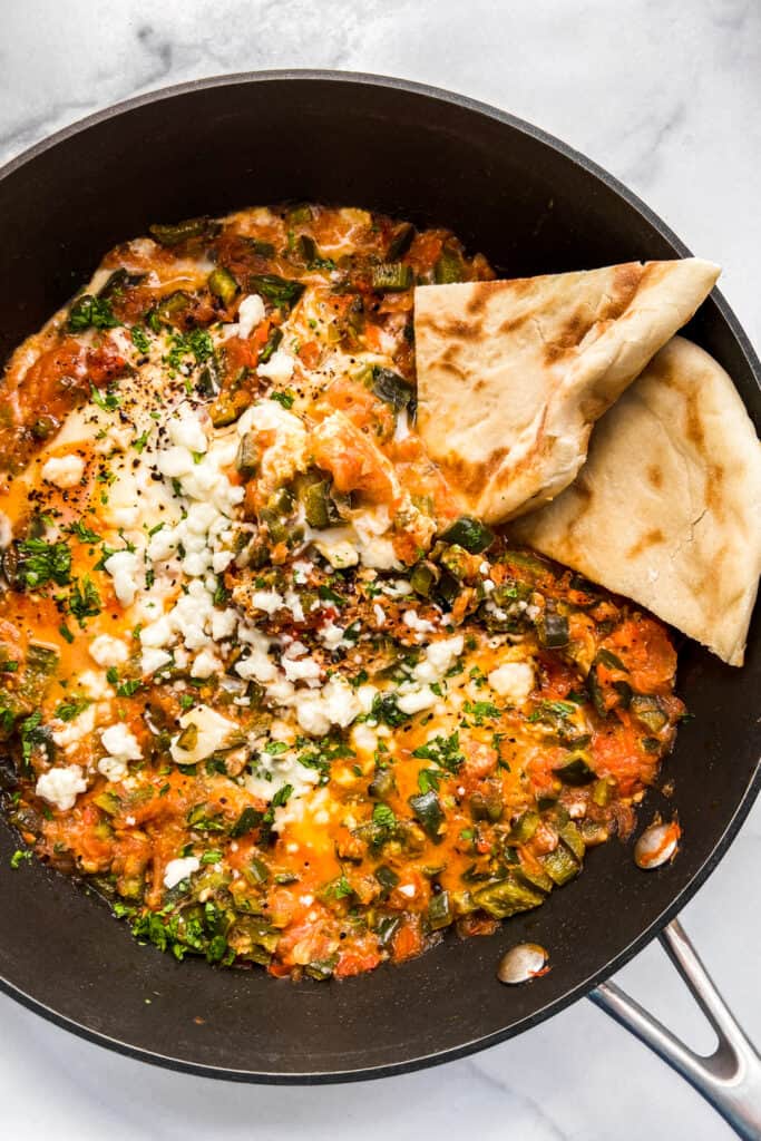 An overhead shot of a large skillet with menemen and slices of pita bread.