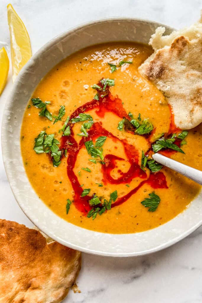 An overhead shot of a bowl of Turkish lentil soup topped with paprika oil and parsley.