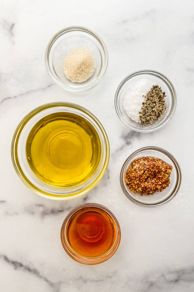 Bowls of olive oil, red wine vinegar, wholegrain mustard, salt, pepper, and sugar on a marble background.