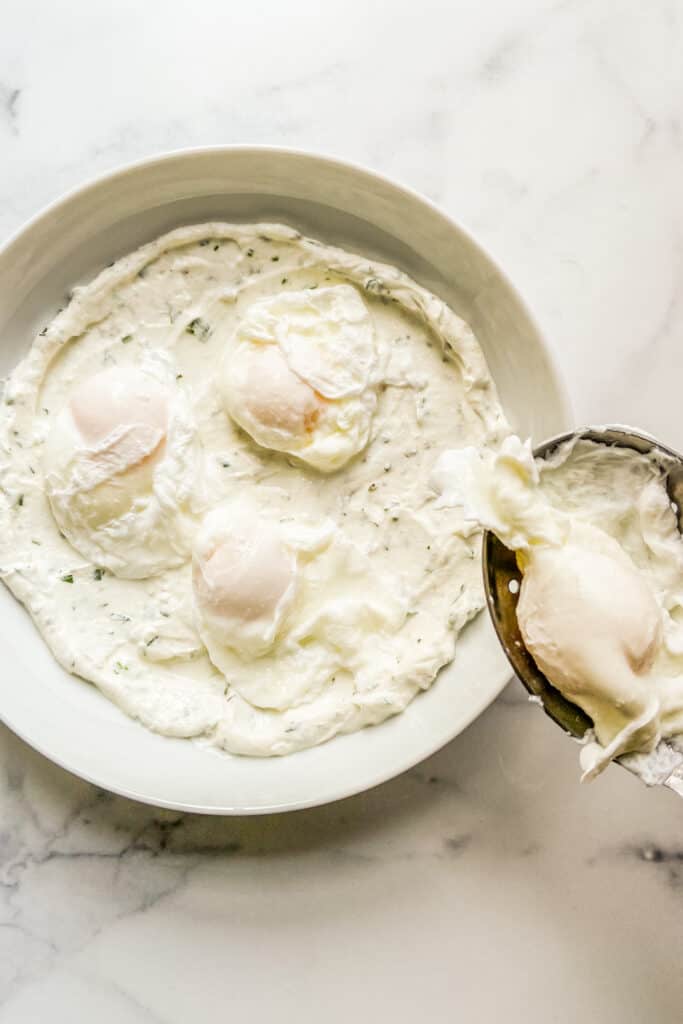 Poached eggs being placed on the bowl of yogurt.