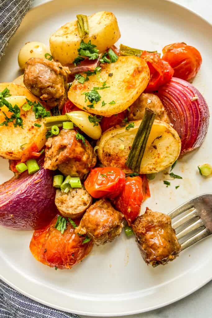 A shot of an off-white plate with potatoes, sausage, and veggies.
