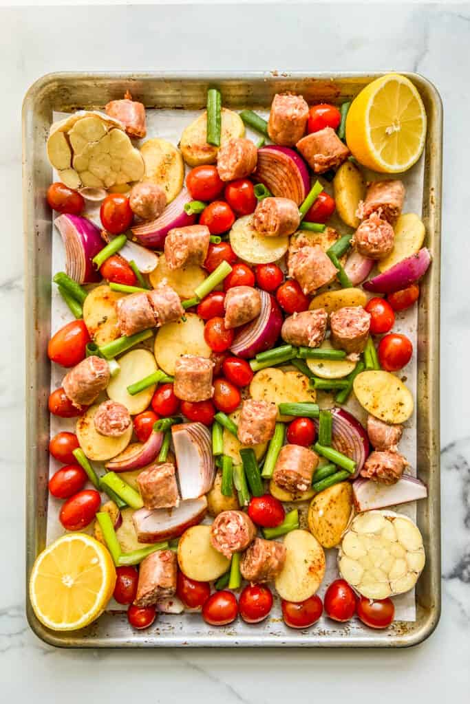 A sheet pan with sausage and chopped veggies, before going in the oven.