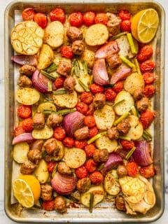 An overhead shot of a tray of roasted Italian sausage, potatoes, tomatoes, and other veggies.