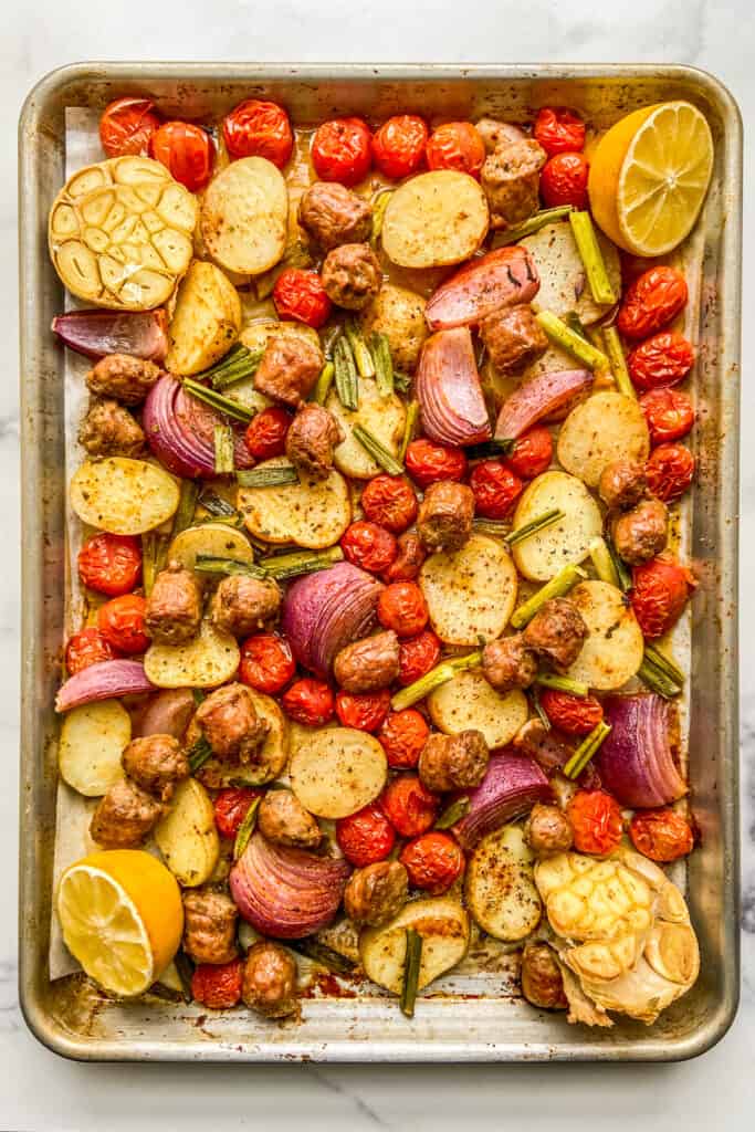 An overhead shot of a tray of roasted Italian sausage, potatoes, tomatoes, and other veggies.