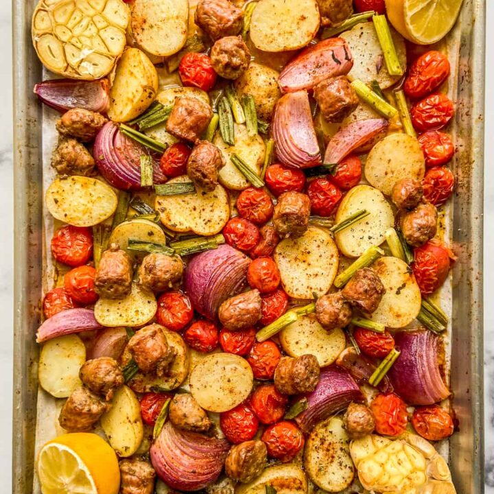 An overhead shot of a tray of roasted Italian sausage, potatoes, tomatoes, and other veggies.