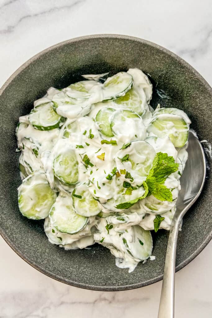 An overhead shot of Turkish cucumber salad in a black bowl with a silver spoon.