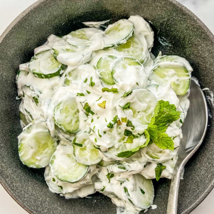 An overhead shot of Turkish cucumber salad in a black bowl with a silver spoon.