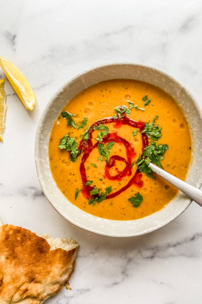 An overhead shot of a bowl of Turkish lentil soup topped with paprika oil and parsley.