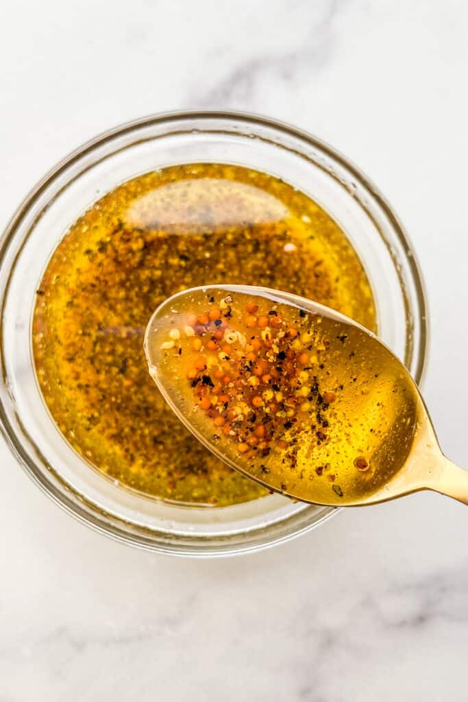 An overhead shot of a wholegrain mustard dressing in a small glass bowl with a gold spoon.