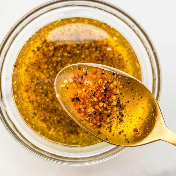 An overhead shot of a wholegrain mustard dressing in a small glass bowl with a gold spoon.