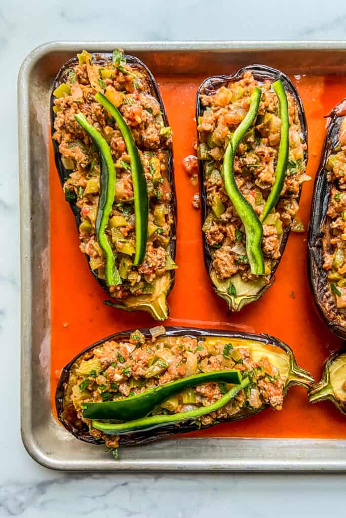 Stuffed eggplants on a baking sheet in a tomato sauce, before going in the oven.