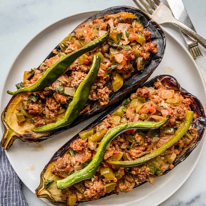 Two stuffed eggplants on a white plate, next to a fork and knife.