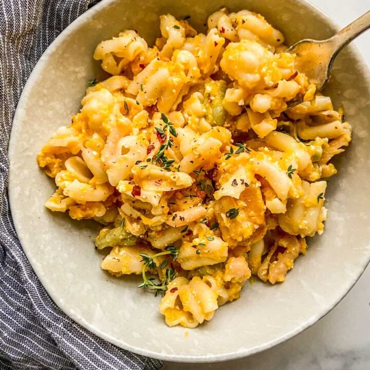 A bowl of butternut squash feta pasta next to a blue and white napkin.