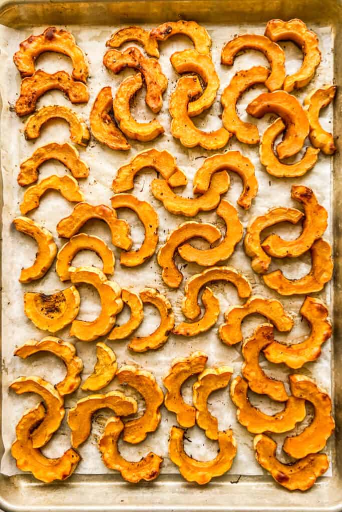 Roasted delicata squash on a parchment lined half sheet pan.