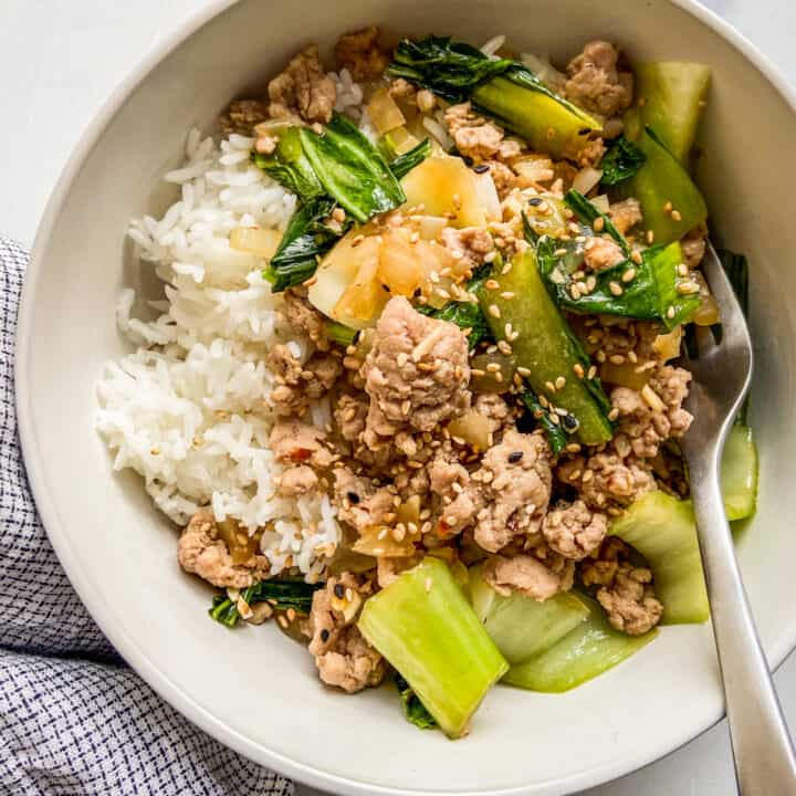 Ground pork stir fry with rice in a white bowl, next to a blue and white napkin.